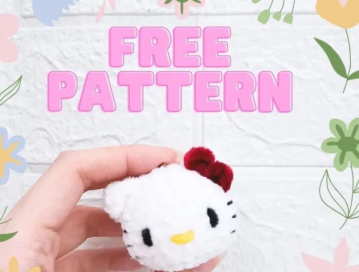 Crochet keychain pattern free hello kitty: white amigurumi Hello Kitty head charm with red bow held in a hand